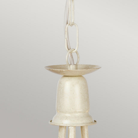 A detailed view of the Minster 3 Light Chandelier in an ivory finish with a gold patina, featuring a smooth metallic bell design and a hanging loop, suspended by a chain against a grey backdrop.