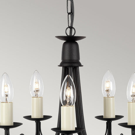 A close-up of the Minster 5 Light Chandelier in a black finish, showcasing its semi-flush fitting and multiple candle-style light fixtures with clear bulb covers, suspended from a chain. The background is smooth and neutral in color.