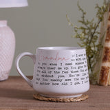 White tapered stoneware mug with a wraparound Grandma verse in black typewriter-style text and pink script, shown on a woven coaster in a home setting.