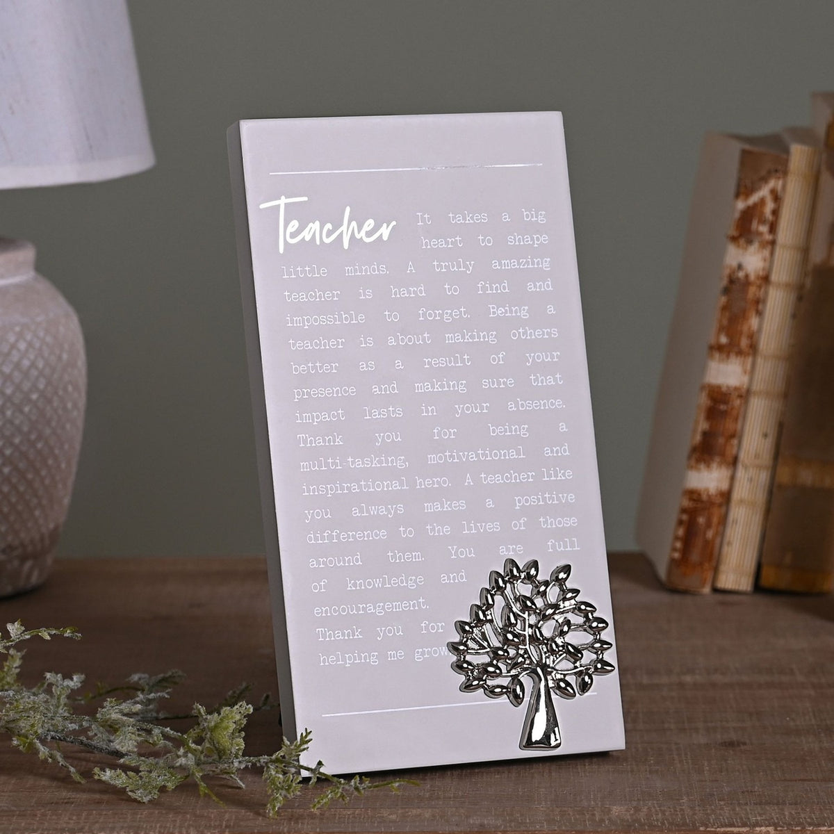 Grey wooden standing plaque with a Teacher verse in white script and a raised silver tree motif, displayed on a wooden surface beside books and a lamp.