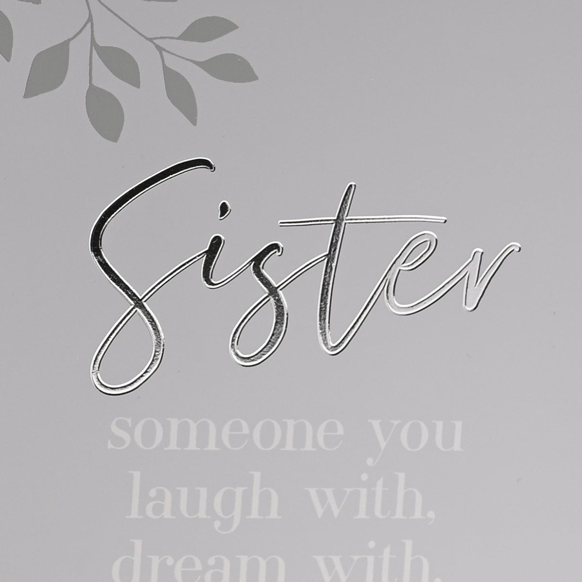 Close-up of the grey hinged photo frame's right panel, showing "Sister" in silver script above a white verse beginning "someone you laugh with, dream with," with a subtle leaf motif in the corner.