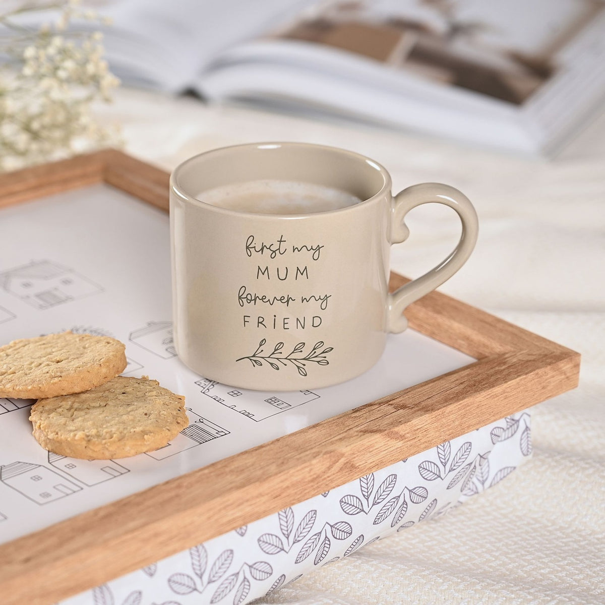 Brown stoneware mug with "first my MUM forever my FRIEND" script and leaf sprig design, filled with coffee and set on a wooden tray with biscuits.
