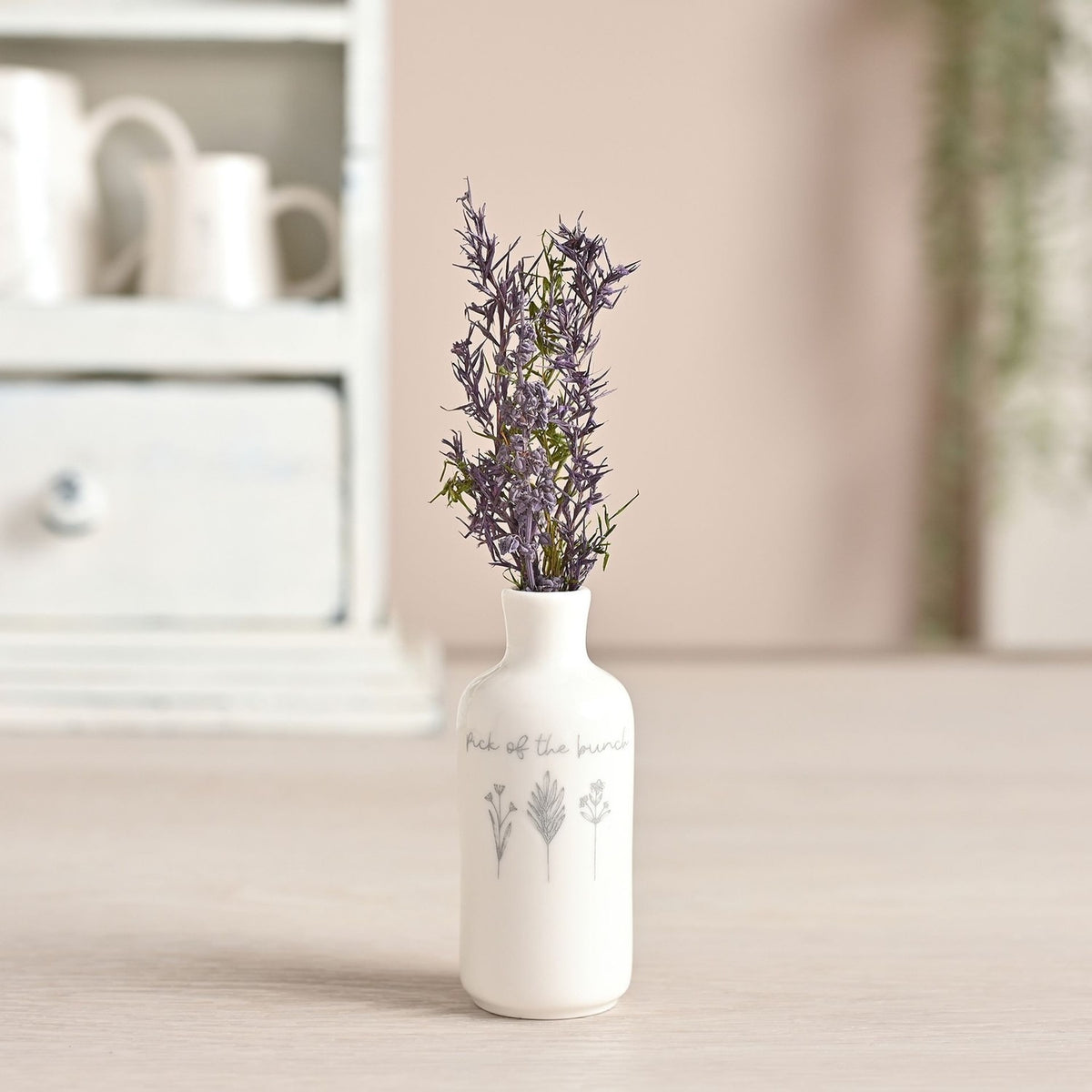Off white ceramic bud vase in a bottle shape with rolled lip, "Pick of the bunch" script and three grey floral line illustrations, shown with dried purple flowers on a wooden surface.