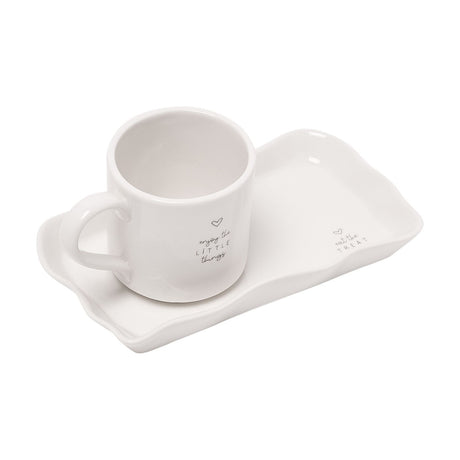 Off-white stoneware mug with rounded handle and heart print "enjoy the LITTLE things", set on a matching wavy-edged rectangular plate, shown on a plain white background.