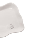 Close-up of an off-white stoneware rectangular plate with a wavy raised rim, printed with a small heart and "eat the TREAT" in fine grey lettering, on a plain white background.