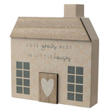 Beige wooden cottage-shaped wall art with a pitched roof, chimney, paned windows, a raised door with a white heart, and the text Love Grows Best in Little Houses.