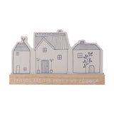Wooden mantel plaque shaped as three grey houses with line-drawn windows and doors, set in a natural wood base reading "Friends Are the Family We Choose," on a white background.