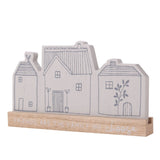 Grey wooden mantel plaque shaped like three houses with line-drawn windows, doors and chimneys, set on a natural wood base reading "Friends Are The Family We Choose," against a plain white background.