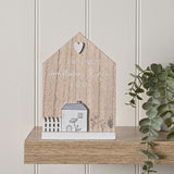Wooden house-shaped plaque with pointed roof and white heart, reading "If friends were flowers I'd pick you" above a white cottage, fence, and florals, displayed on a wood shelf near a plant.