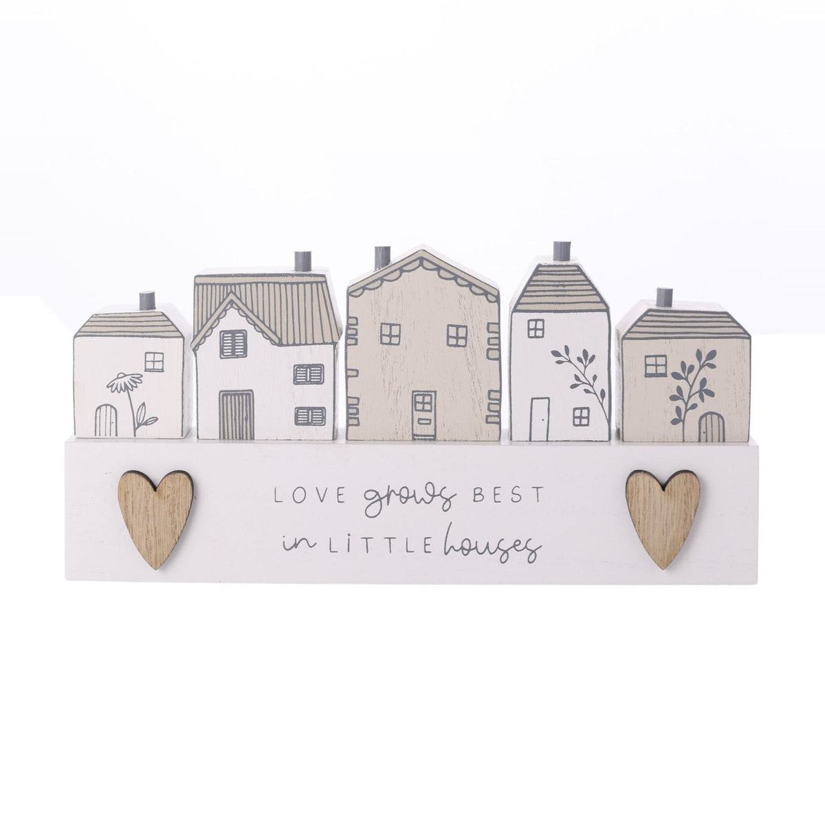Wooden wall plaque with five little houses in white and beige with grey chimneys and door motifs, two wood-toned hearts and "Love grows best in little houses" text, set on a plain white background.
