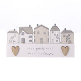 Wooden wall plaque with five little houses in white and beige with grey chimneys and door motifs, two wood-toned hearts and "Love grows best in little houses" text, set on a plain white background.