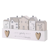 Wooden plaque with five white and beige houses, grey line details, chimneys, wood-toned hearts, and the text Love grows best in little houses on a plain background.