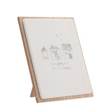 Grey wooden plaque with easel stand featuring three line-drawn houses, hearts, and the text Love grows best in little houses on a white panel with natural wood border.