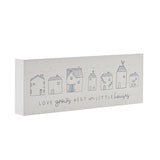 White wooden mantel plaque with a row of seven line-drawn houses and "LOVE grows BEST in LITTLE houses" text in grey, shown at an angle on a plain background.