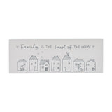 White wooden mantel plaque reading "Family is the heart of the home" in grey script, above a row of seven line-drawn houses with hearts and floral details.