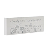 White wooden mantel plaque reading "Family is the heart of the home" in grey script above a row of seven line-drawn houses, shown at an angle on a plain background.