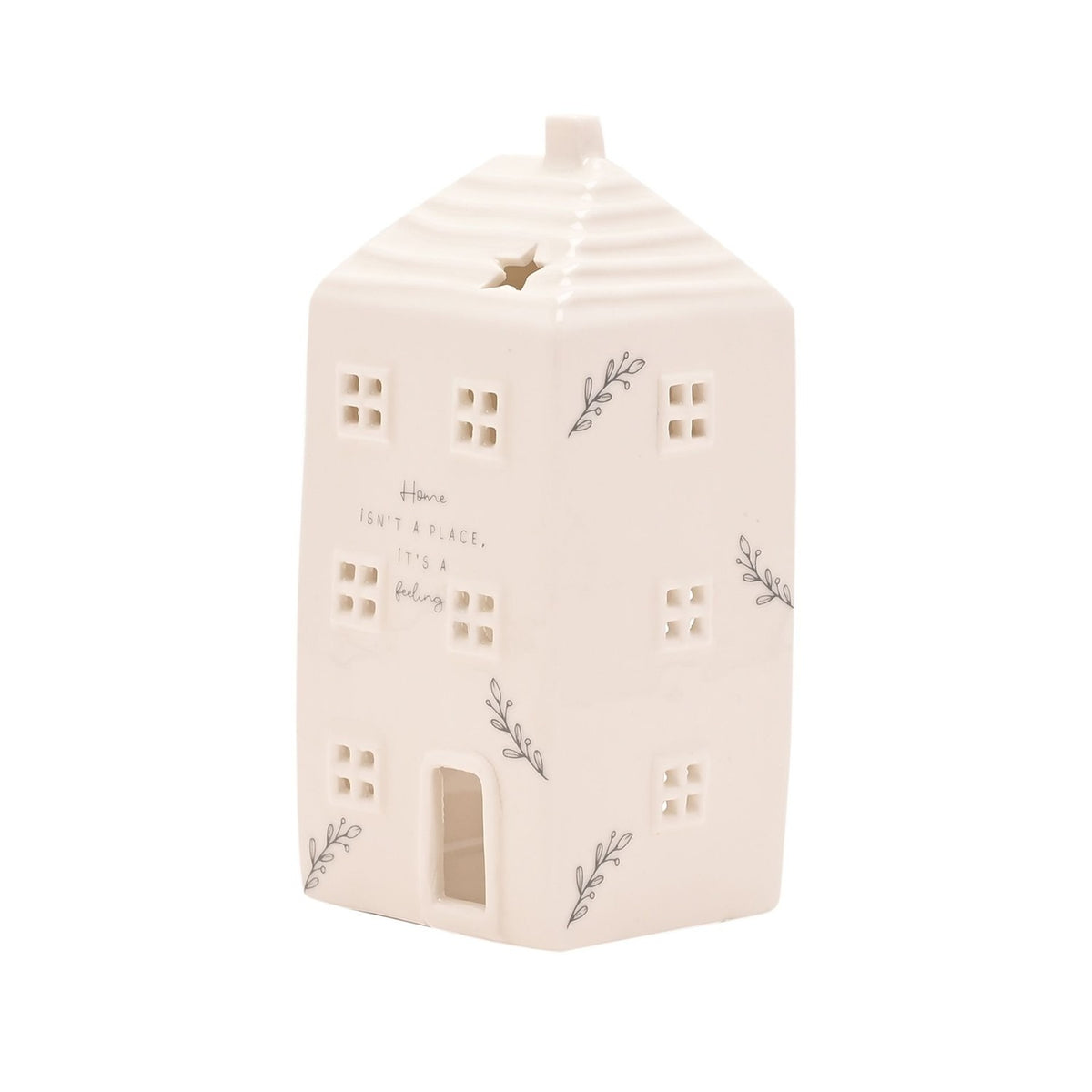 White ceramic house-shaped tea light candle holder with ridged roof, chimney, star cut-out, cut-out windows, door, and grey "Home isn't a place" lettering, on a plain background.