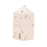 White ceramic house-shaped tea light candle holder with ridged roof, chimney, star cut-out, cut-out windows, door, and grey "Home isn't a place" lettering, on a plain background.