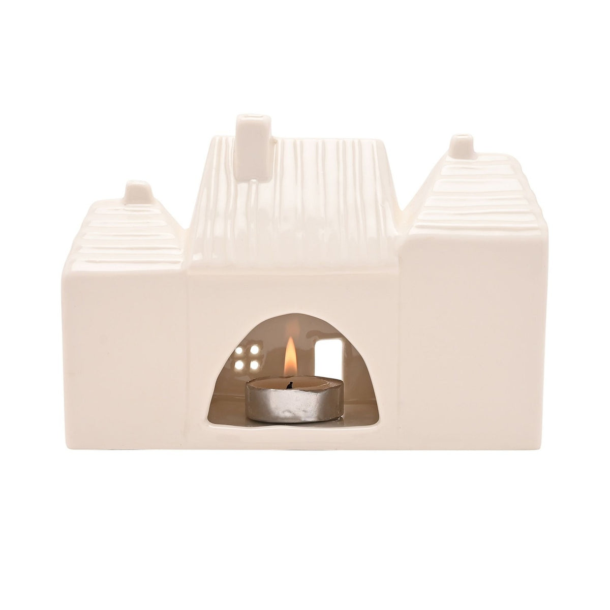White ceramic tea light candle holder shaped like three terraced houses with ribbed roofs, chimneys, and cut-out windows, lit tealight glowing inside on a plain background.