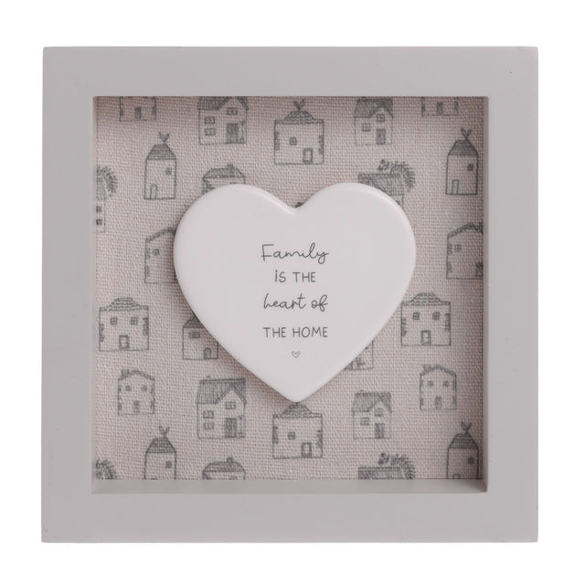 Square off-white wooden framed wall plaque, 15x15cm, with a raised white heart reading "Family is the heart of the home" over a printed grey house pattern background.