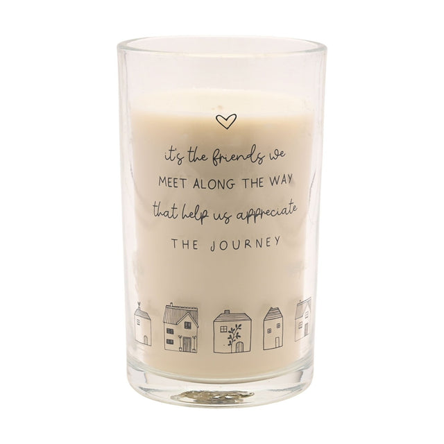 Tall scented candle in a clear glass jar with cream wax, printed with a heart, friendship quote, and a row of line-drawn houses, shown on a plain white background.