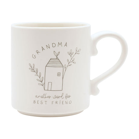 Cream ceramic mug with curved handle, featuring a line-drawn house between leafy sprigs, "GRANDMA" arched above and "another word for best friend" below, on a plain white background.