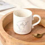 Cream mug with handle printed with "GRANDMA, another word for BEST FRIEND" and a line-drawn house design, hidden script inside the rim, set on a wooden tray with a spoon.