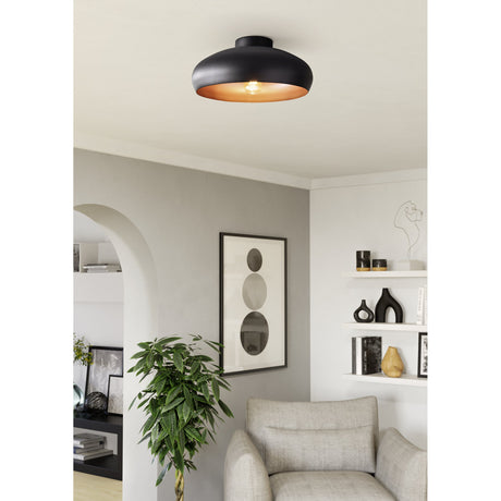 Mogano Ceiling Light in matt black with copper-coloured lining, a wide flush steel dome shown fitted above a living room seating area with an armchair and shelving.