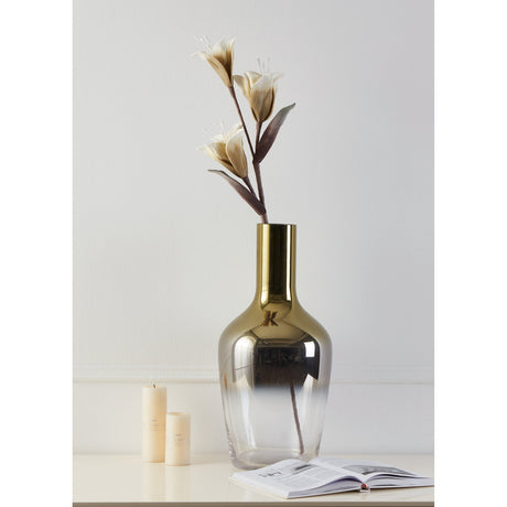 Molave Artificial Flower in brown and white, a tall single stem with three lily-like blooms, displayed in a gold and smoked glass vase on a sideboard with candles and an open book.