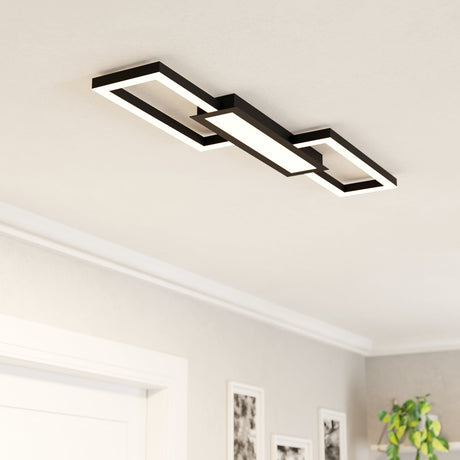 Monirote LED flush ceiling light in black, featuring two offset rectangular frames bridged by a central panel with white diffused LED strips, shown mounted in a hallway ceiling.