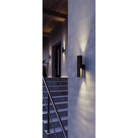 Montelauro LED Outdoor Wall Light in black aluminium, slim cylinder design casting up and down light, shown mounted on an exterior wall near a staircase at dusk.