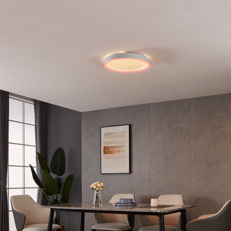 Montemorelos round LED flush ceiling light in white, 42cm, with warm glow and pink-toned edge accent, shown installed above a dining table in a grey-walled dining room.