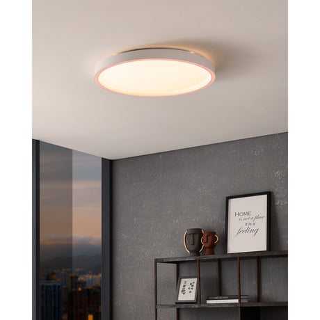 Montemorelos round LED flush ceiling light in white aluminium with a crystal-effect diffuser glowing with a pink-toned edge, shown installed on a hallway ceiling.