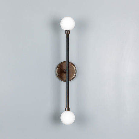 Monto Twin Glass Globe Wall Light IP44 with a slim antique brass rod on a round wall plate, two opal glass globes at top and bottom, shown against a plain light grey background.