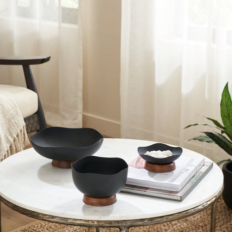 Monywa Metal Decorative Bowls in black with wavy rims on round wood bases, shown in three sizes on a marble coffee table in a living room.