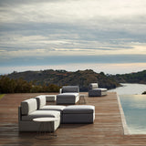Mood XL upholstered garden corner sofa module in light grey fabric, shown as part of a modular outdoor seating arrangement on a wooden deck beside a pool with a coastal view.