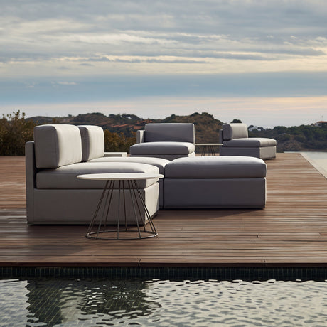 Mood XL armless centre module garden sofa in light grey outdoor fabric, upholstered base with matching seat and back cushions, shown on a wooden poolside deck with matching lounge chairs.
