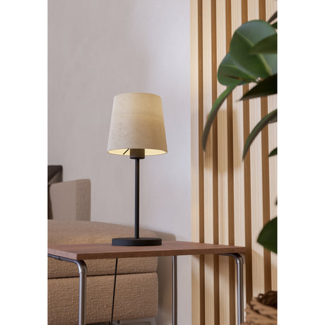 Morbarne Table Lamp in black with a slim steel stem, round base, and tapered off-white fabric shade, shown on a side table in a living room setting.