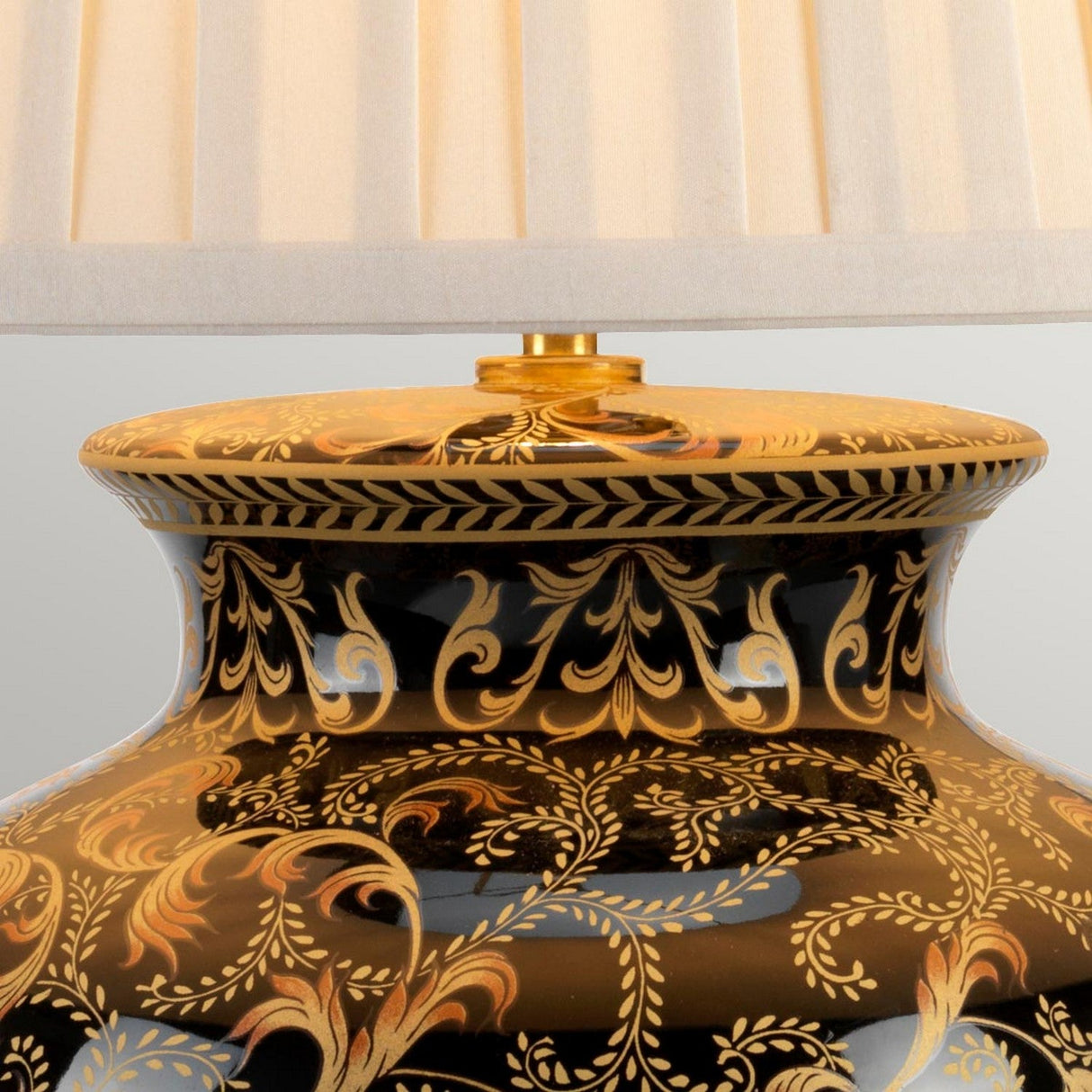 Close-up of the ornate Morris 1 Light Large Table Lamp in gold and black, featuring an intricate floral pattern on its ceramic base. The lamp is complemented by a pleated beige lampshade, adding elegance and a touch of class to this decorative piece.