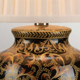 Close-up of the Morris 1 Light Small Table Lamp in gold and black, featuring a floral patterned ornate base with gold and orange designs set against a dark background. A cream-colored pleated lampshade is partially visible at the top, enhancing its elegance.