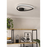 Moschella LED flush ceiling light in black, an open rounded-triangle ring with white LED diffuser edge, mounted flush to a light grey ceiling above a wooden shelving unit with decor.