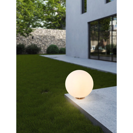 Mosvine Outdoor Post Light 30cm in white, a spherical frosted globe on a low round base, illuminated on a stone ledge beside a lawn and modern house exterior.