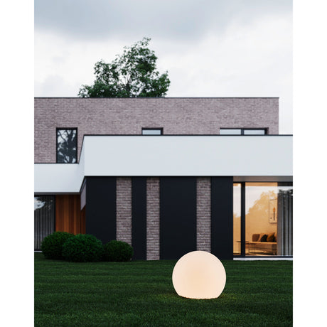 Mosvine Outdoor Post Light 39cm in white, a glowing spherical globe light on a modern garden lawn in front of a brick and dark-panelled house.