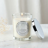 Lit 21st Birthday sandalwood scented candle in a glass jar with cream wax, silver medallion, and matching lid, set on a marble surface.
