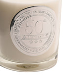 Close-up of the 50th Birthday Sandalwood Scented Candle in a clear glass jar with a round silver medallion engraved "50th Birthday" and time milestones, set against a white background.