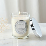 Lit 70th Birthday sandalwood scented candle in a clear glass jar with round silver medallion, shown with its silver lid beside it on a marble surface.
