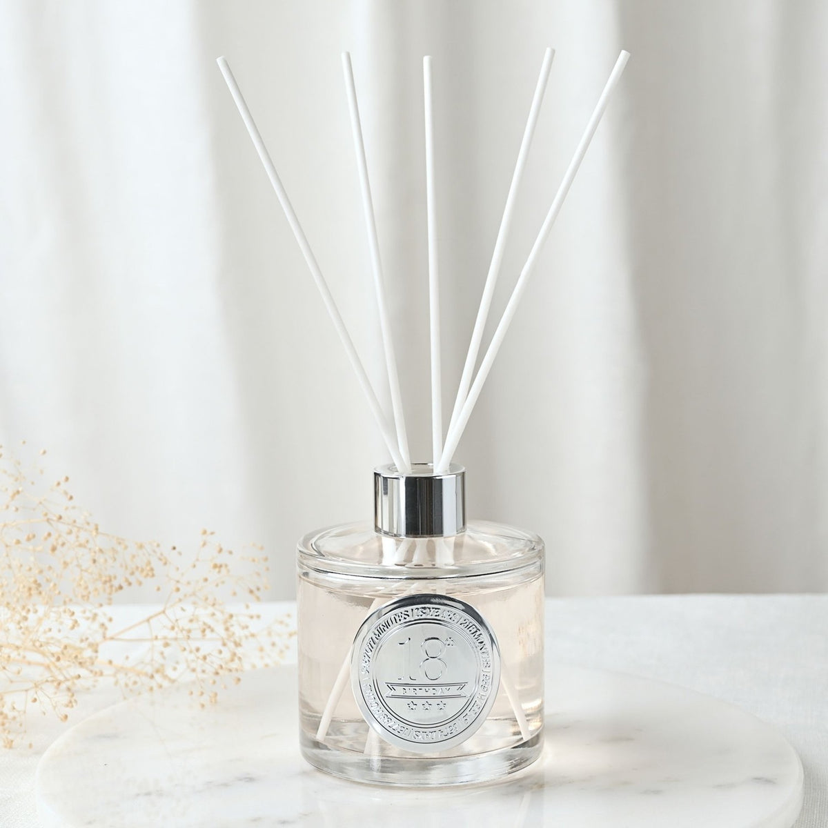 18th Birthday Sandalwood Reed Diffuser 200ml in a round clear glass bottle with silver collar and white reeds, with a silver number 18 seal, set on a marble surface.