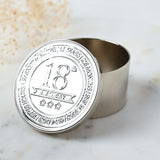 Round silver metal trinket box with embossed "18th Birthday" lid, ribbon banner and stars, time-in-numbers band around the edge, shown open on a marble surface.