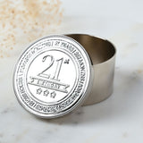 Round silver metal trinket box with open lid embossed "21st Birthday" and three stars, bordered by a time-count inscription, shown on a marble surface.