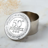 Round silver metal trinket box with embossed lid reading "50th Birthday" and star details, shown open to reveal a polished interior, set on a marble surface.